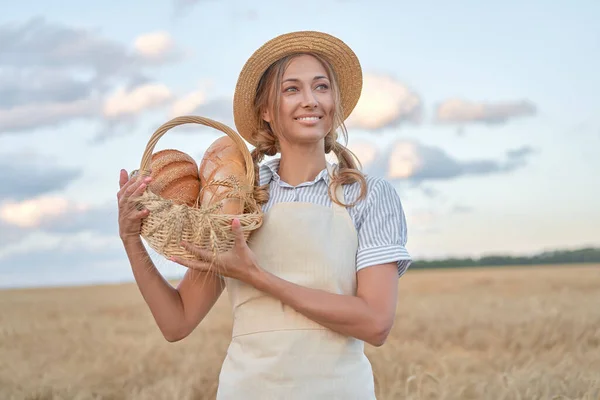 Female farmer standing wheat agricultural field Woman baker holding wicker basket bread eco product Baking small business Caucasian person dressed straw hat apron organic healthy food concept