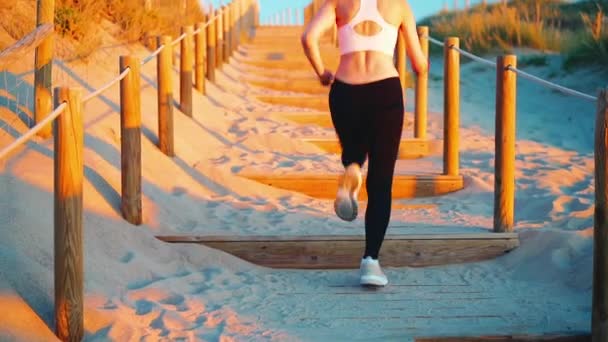 ビーチ木製の階段のパススローモーションで実行されているアスレチックスポーツ女性 海辺で健康的なライフスタイルを楽しむ若い大人の白人女性のジョギング屋外 夏のアクティブライフスタイル — ストック動画