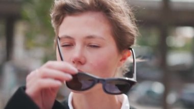 Güneş gözlüklü güzel beyaz kadın sonbahar siyah ceketini dışarıda giydi. Sonbaharda şehir caddesinde şık, sevimli bir bayan. Orta yaşlı güzel yüzlü bir kadın.