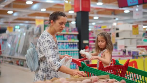 娘はスーパーマーケットのトロリーに座って スーパーで果物や野菜を買っている素敵な家族 母親と小さな娘 菜食主義と健康的な食事の概念 ファミリー食料品店 — ストック動画