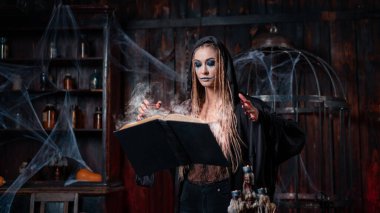 Cadılar Bayramı konsepti Kara başlıklı cadı karanlık zindan odasında sihirli büyü yapmak için sihirli bir kitap kullanıyor. Dişi büyücü büyücüsü. Büyü kitabı içiyorum.