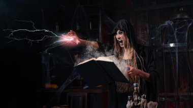 Cadılar Bayramı konsepti Kara başlıklı cadı karanlık zindan odasında yıldırımla büyü yapmak için sihirli kitap kullanıyor. Dişi büyücü büyücü Gotik iç mimari Elini öne koydu çığlık çığlığa