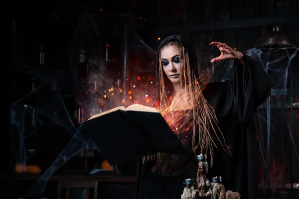 ハロウィンのコンセプト 魔法の呪文を想起させる魔法の本を使用して黒フード立って暗いダンジョンルームに身を包んだ魔女 火は魔法の輝き女性のネクロマンサーウィザードゴシックインテリア — ストック写真