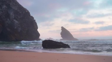 Okyanusun vahşi kumsal fırtınalı havasında gün batımı. Praia da Adraga kumlu plajı, manzaralı arka plan, Sintra Cascais Portekiz el bilgisayarı etkisi. Mavi enerjinin ve berrak okyanus suyunun canlılığı