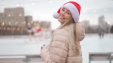 Winter, Mutlu kadın Noel Baba şapkası takıp şehrin dışında duruyor ve gülümsüyor. Noel zamanı. Olumlu gülümseyen beyaz kadın. Orta yaşlı kadın. Arkanı dön ve Noel tatiline davet et.