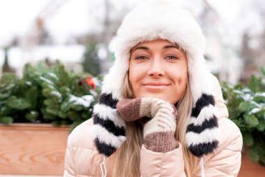 Kış portresi genç yetişkin güzel sarışın kadın komik pofuduk şapkalar giyiyor. Noel havası. Kar yağan kış güzellik moda konsepti. Güzel orta yaşlı kadın Noel çelengi yakınlarında dışarıda oturuyor.