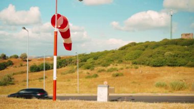 Rüzgar çorap sineği. Sıcak bir yaz günü, terk edilmiş rüzgârlı bir hava alanında, rüzgâr esiyor ve rüzgârlık tembellik ediyor. Rüzgâr Sock bulutlu gökyüzü dağı ve arka planda arabalı yol 