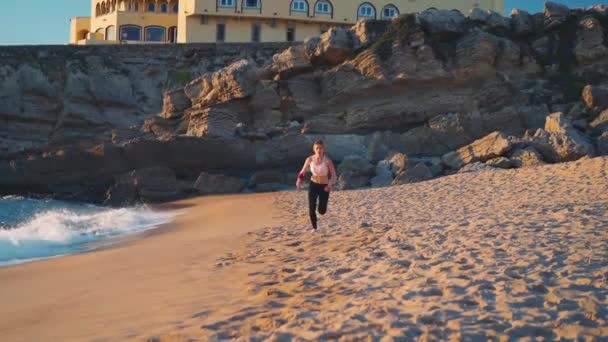 海のビーチを走るスポーティブロンドの女性 若い白人女性は屋外でランニング海岸を行使します 健康的なランニングと屋外運動の概念 アクティブ スポーティアスリートジョギング 夏休み — ストック動画
