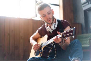 Akustik gitar çalan yakışıklı genç adam oturma odasında beyaz tenli erkek hippi kulaklıkçı şarkı söyleyen, müzik dinleyen, yaratıcı, genç adamı rahatlatan, orta yaşlı adam.