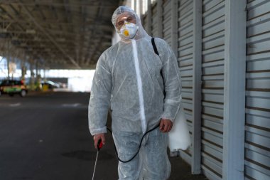 Koruyucu giysi giyen işçiler dezenfekte ekipmanları halka açık bir yerde park ediyorlar. Genel olarak dezenfektan güvenliği ve solunum maskesi Covid salgını önleyici tedbirler