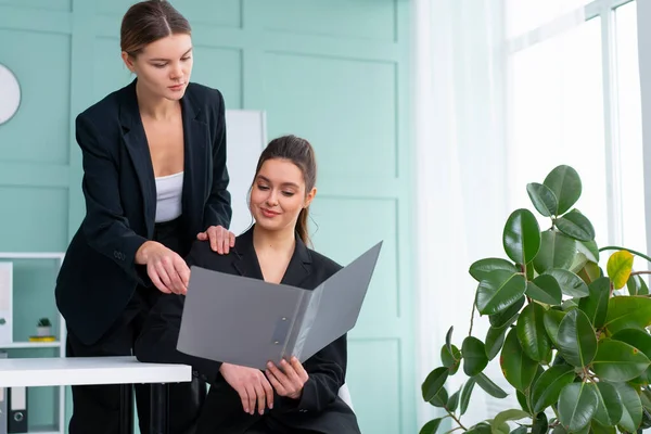 Young women leaders are checking financial statements from paper documents. Two female confident business worker dressed black suit in office checking financial document looking folder and discussing