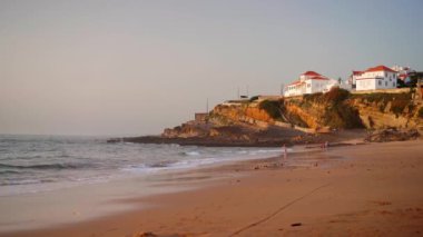 Portekiz 'in Colares şehrindeki Praia das Macas Elma Plajı. Gün batımından önceki fırtınalı bir günde. Okyanus kıyısında küçük bir şehir.