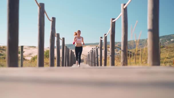 田径女运动员在海滩上跑木径慢动作跟踪镜头 可敬的年轻成年白人女性在海滨慢跑 享受着健康的生活方式 夏天的活跃生活 — 图库视频影像