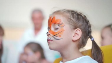 Çocuklar boyayla yüzleşir. Çocuklar için düzenlenen karnaval partisinde küçük bir kızın yüzünde özel vücut boyası ve özel kaplan maskesi olan sanatçı resmi. Çocuklar için vücut resimleri..