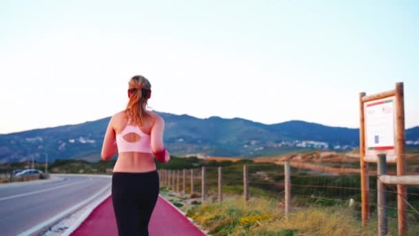 全景体育女慢跑者跑自行车道附近的道路与山区背景 活泼的女人慢跑的天性 健康的生活方式概念 运动服 夜间训练 — 图库视频影像