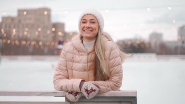 Wintertime. Happy adult woman on winter city street dressed winter clothes and white knitted hat. Positive caucasian female winter outdoor showing thumb nail. Christmas holiday concept.