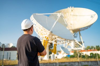Engineer looking earth based astronomical radio telescope. Radio telescopes used in science for space observation and distant objects exploring. Caucasian man white protective helmet satellite dishes