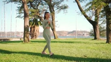 Fitness woman 20s in sports wear doing lunges, and stretching legs on summer park near seaside. Warm up before jogging workout. Athletic female jogger training legs. Squat lunges training