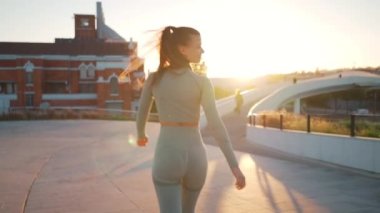Back view view of sportive woman walking on street. Fit caucasian female dressed sportive wear confidence walking on park near seaside sunny summer day. Athletic young woman walk Healthy lifestyle