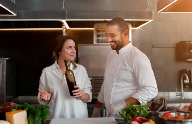 Yakışıklı genç Afrikalı şef, beyaz kız arkadaşıyla mutfakta kırmızı şarap malzemesi kullanarak yemek pişiriyor. Bir aşçı bir kıza nasıl yemek yapılacağını öğretir. Erkek ve kadın profesyonel mutfakta yemek pişiriyor..