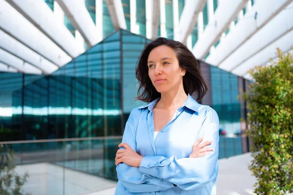Confidence Businesswoman portrait with crossed hands. Pretty business woman 30 years old standing near office building dressed blue shirt. Caucasian female business person outside