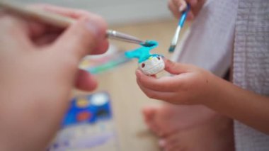 Caucasian child girl painting watercolor paint on small ceramic figure with father close up hands. Kids arts and crafts creative activity class at home. Little girl make ceramic decor sitting floor 