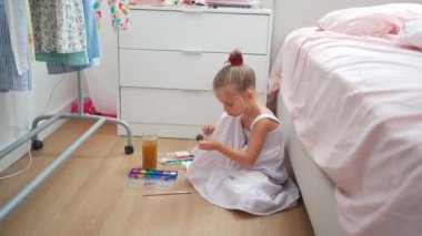 Caucasian child girl is painting watercolor paint on small ceramic figure with fun. Kids arts and crafts creative activity class at home. Little girl make ceramic decor sitting floor 