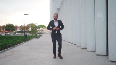 Businessman walking city street fasten buttons near modern office building. Confident guy in suit being on his way to job. Portrait of business man commuting to work. Slow motion. Handheld. 