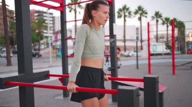 Paralel barlara triseps bandıran sportif formda bir kadın. Çekici beyaz kadın koşudan önce ısınıyor. Spor egzersizleri parktaki spor sahalarında açık hava. Güzel, sportif kadın..