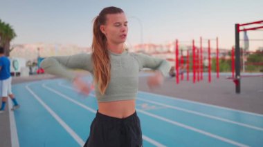 Kadın koşmadan önce kollarını esnetiyor ve ısıtıyor. Formda sporcu bir kadın ısınmak için koşu pistinde koşuya hazırlanıyor. Atletik kadın antrenmana hazırlan.