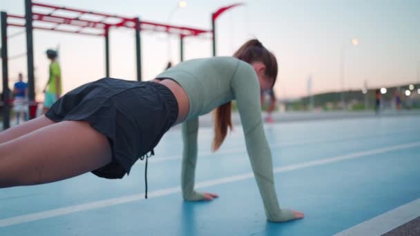 女运动员在体育场跑道上训练 年轻的女运动员做俯卧撑作为运动训练的一部分 女子运动服训练 黄昏时分的运动女子仰卧起坐练习 — 图库视频影像