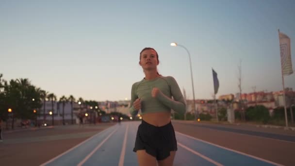 女运动员在运动场附近的跑道上跑步 适合高加索的年轻女子在黄昏慢跑时在跑道上跑步 户外运动女慢跑者的训练 健康生活方式概念 — 图库视频影像