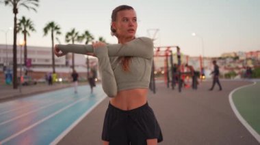 Koşu parkurunda koşmadan önce esneme ve ısınma hareketleri. Formda sporcu kadın vücudunu ısıtıyor. Yaz akşamları spor giyinen kız dışarıda egzersiz yapıyor. 