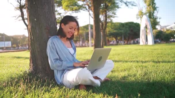 Šťastná Brunetka Žena Pomocí Notebooku Zatímco Sedí Stromu Trávě Parku — Stock video