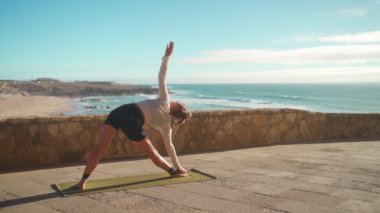 Arka planda okyanus manzaralı yoga egzersizleri. Kafkasyalı formda bir kadın deniz kıyısında yoga eğitimi alıyor. Sağlıklı yaşam tarzı kavramı. Yetişkin bir kadın yoga ve esneklik eğitimi alıyor.. 