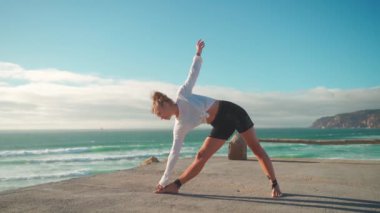 Arka planda okyanus manzaralı yoga egzersizleri. Kafkasyalı formda bir kadın deniz kıyısında yoga eğitimi alıyor. Sağlıklı yaşam tarzı kavramı. Yetişkin bir kadın yoga ve esneklik eğitimi alıyor.. 