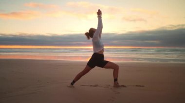 Gün batımında okyanus manzaralı yoga egzersizleri. Beyaz kadın deniz kıyısında yoga eğitimi alıyor. Sağlıklı yaşam tarzı kavramı. Yetişkin bir kadın yoga ve esneklik eğitimi alıyor. Savaşçı pozu