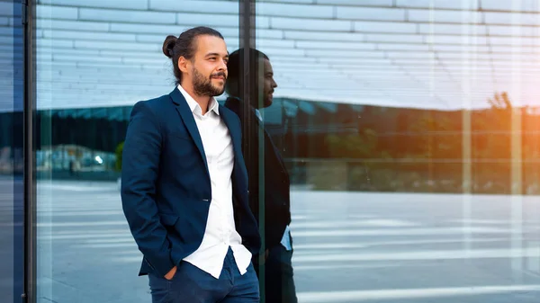 Successful businessman in suit with beard standing near office building confidently looking away. Hispanic male business person side view portrait. Web banner Free space. Modern Business people
