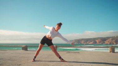 Arka planda okyanus manzaralı yoga egzersizleri. Kafkasyalı formda bir kadın deniz kıyısında yoga eğitimi alıyor. Sağlıklı yaşam tarzı kavramı. Yetişkin bir kadın yoga ve esneklik eğitimi alıyor.. 