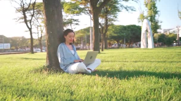 Šťastná Brunetka Žena Pomocí Notebooku Zatímco Sedí Stromu Trávě Parku — Stock video
