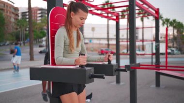 Fitness, spor, sportif insanlar konsepti. Açık spor salonunda paralel barlarda karın egzersizi yapan genç bir kadın. Kafkas fitness kadın antrenman kasları spor sahasında. 