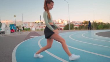 Spor yapan 20 'li yaşlarda spor yapan kadınlar hamleler yapar ve koşu pistinde bacaklarını esnerler. Koşu antrenmanından önce ısın. Atletik bayan koşucu bacakları çalıştırıyor. Çömelme eğitimi aldı