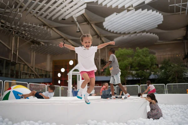 Happy little girl jumping in pool with white plastic balls in amusement park. playground for kids. Active leisure for children.