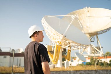 Engineer looking earth based astronomical radio telescope. Radio telescopes used in science for space observation and distant objects exploring. Caucasian man white protective helmet satellite dishes