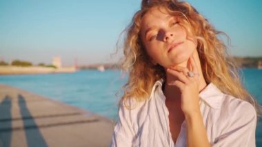 Sarışın kıvırcık kız öpücük yolluyor. Beyaz gömlek giyen, mutlu görünen, hava öpücüğü, aşk konsepti gönderen bir kadın. Amerikan genç bayan setin kenarında güneşli bir yaz günü kameraya dokunuyor. 