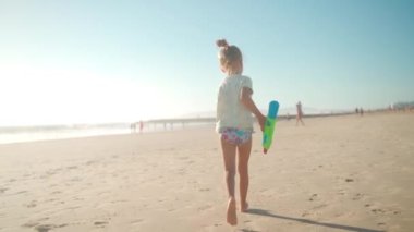 Çocuk yaz günü su tabancasıyla okyanus kumsalı oynuyor. Küçük beyaz kız elinde su tabancasıyla kumsalda koşuyor. Sevimli bayan. 5 yaşında. Kumsalda el kamerasıyla oynamaktan zevk alıyor.. 