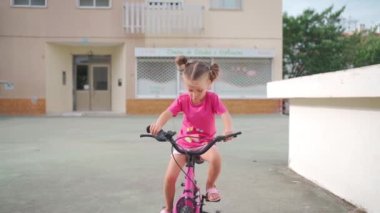 Güneşli bir yaz gününde şehirde bisiklet süren sevimli, gülümseyen bir kız. Çocuklarla aktif aile eğlencesi. Küçük beyaz kız 5 yaşında Pembe çocuk bisikletiyle eğlen