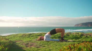 Arka planda okyanus manzaralı yoga egzersizleri. Kafkasyalı formda bir kadın deniz kıyısında yoga eğitimi alıyor. Sağlıklı yaşam tarzı kavramı. Yetişkin bir kadın yoga ve esneklik eğitimi alıyor.. 