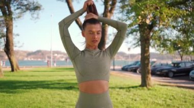 Genç bir kadın spor antrenmanından önce saçını at kuyruğuna takıyor. Yavaş çekim spor ve spor. Beyaz saçlı genç bir kadın at kuyruğu takıyor spor kıyafetleri giyiyor yaz parkının arka planında dikiliyor.