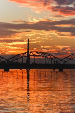 Güzel günbatımı gökyüzü ve onların yansımaları geniş bir nehrin sakin sularında. İki köprü görünürde..